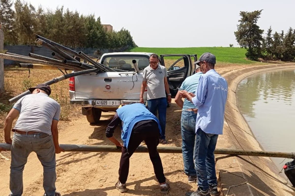 Agents de la Police de l'Eau chargeant des tuyaux saisis dans un pick-up, au bord d'un bassin d'irrigation